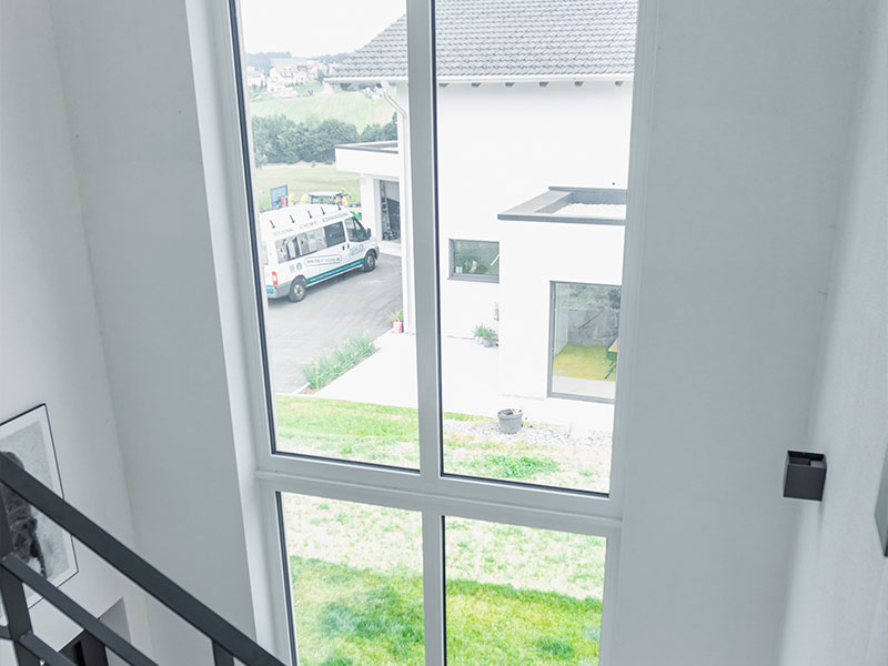 Großes Treppenhausfenster in weiss mit Ausblick auf einem Garten und zum Nachbargrundstück