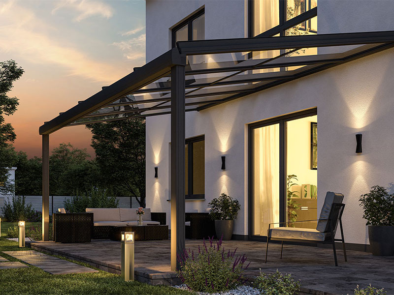 Schwarze Glasüberdeckung über einer Terrasse in der Sonnendämmerung mit Gartenlichtern