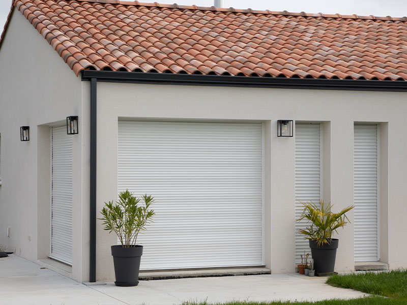 Haus Hinterseite mit Terrassenfenstern, runtergezogene Rollläden. Im Vordergrund zwei Planzen im Blumentopf.
