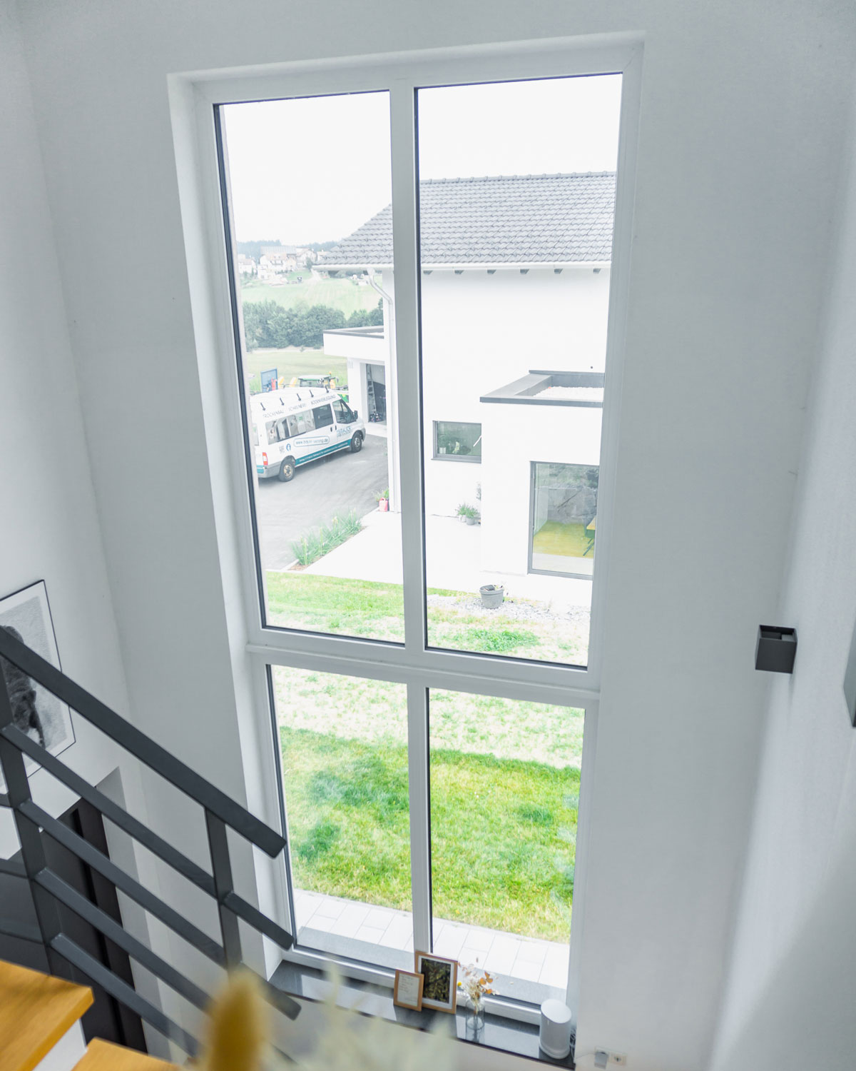 Großes Treppenhausfenster in weiss mit Ausblick auf einem Garten und zum Nachbargrundstück
